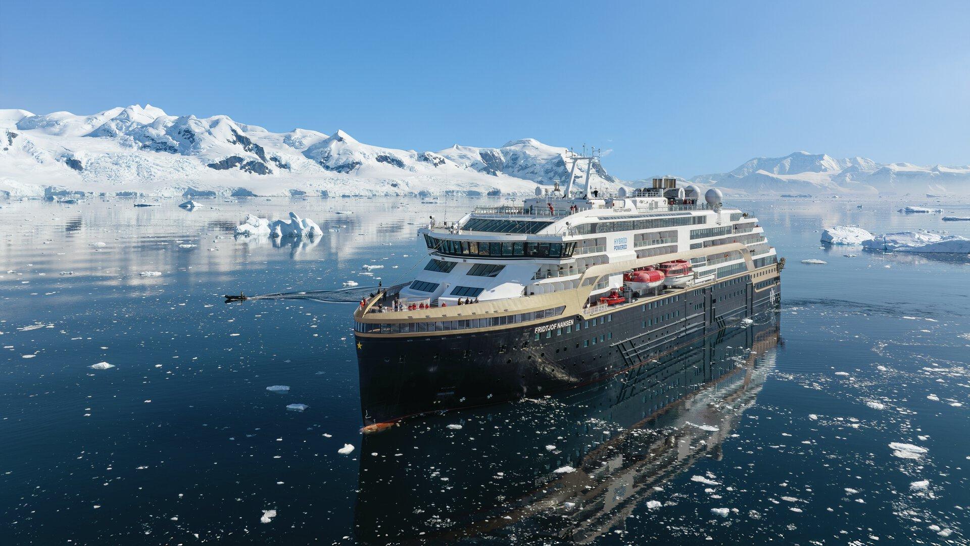 HX Expeditions ship Fridtjof Nansen among sea ice below snowy mountains in Antarctica