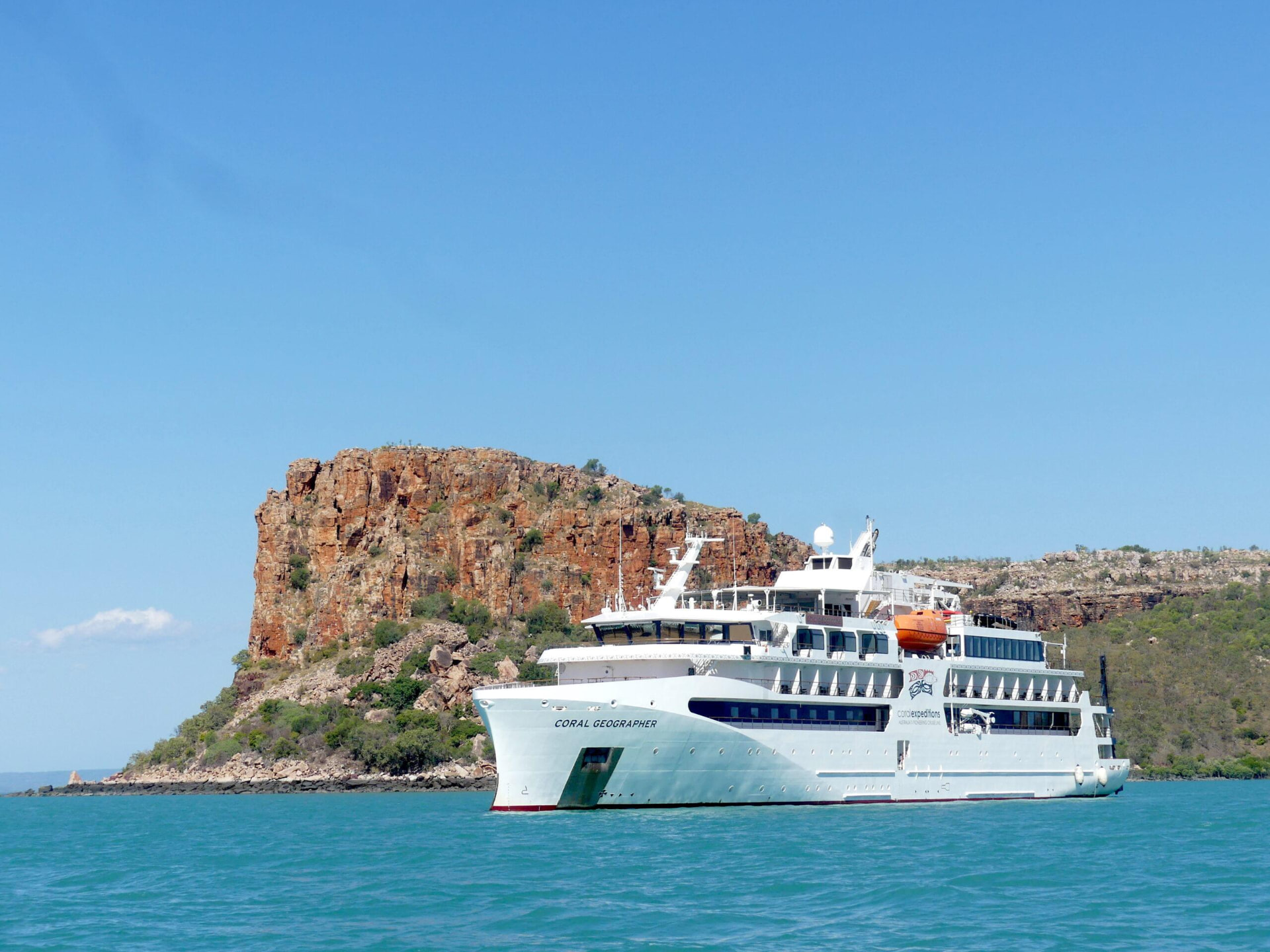 Coral Expeditions ship Coral Geographer below red cliffs on the Kimberley coast of Australia