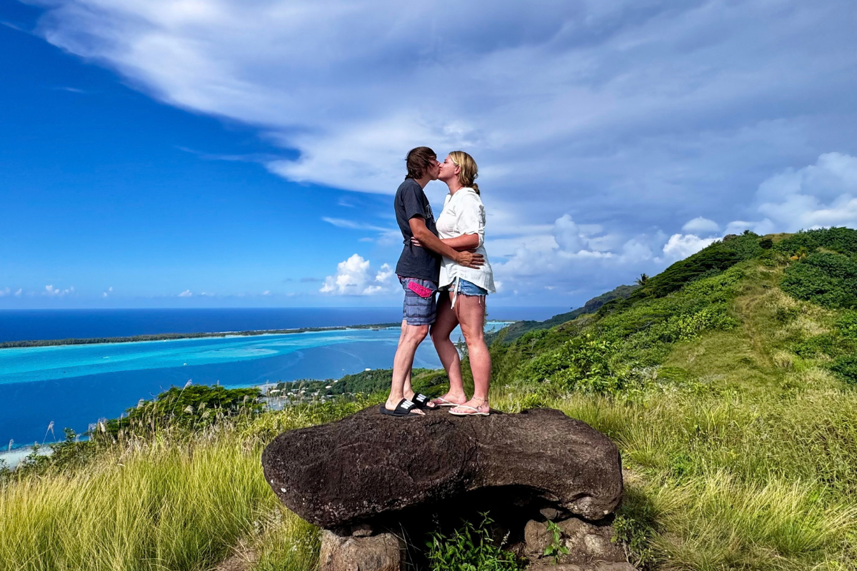 Couple kissing on a hilltop above a turquoise lagoon in French Polynesia