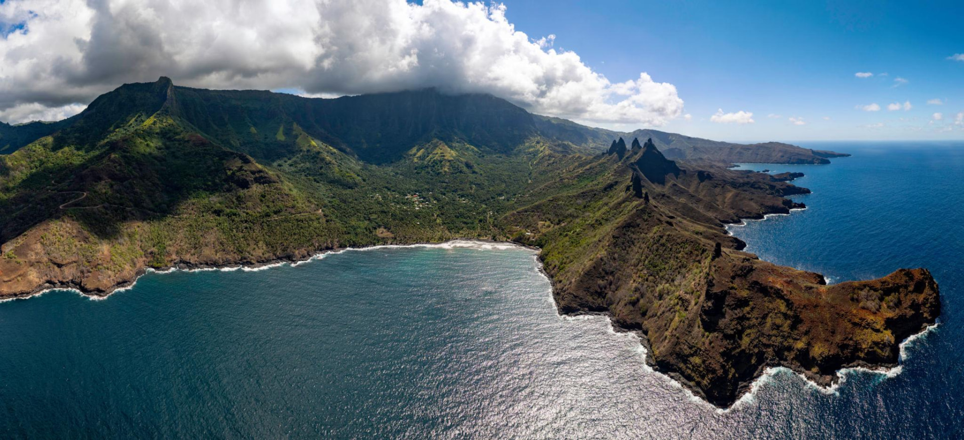 Aerial view of the Marquesas, French Polynesia, with rugged green mountain ridges and a rocky coastline beside the Pacific Ocean