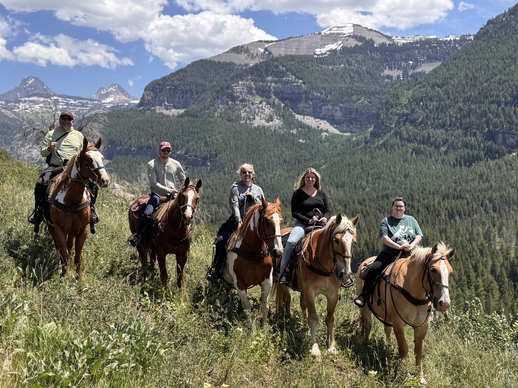 Horseback riders in the mountains of Montana, with snowy peaks behind