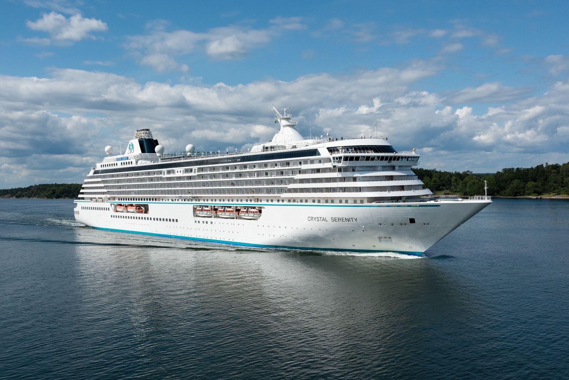 Crystal Serenity sailing past a wooded coastline under a blue summer sky