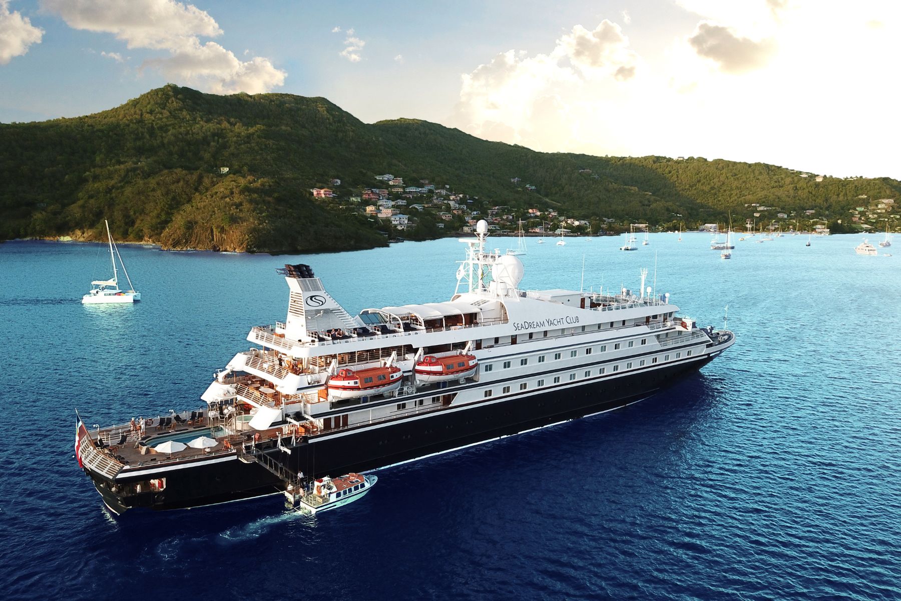 SeaDream Yacht Club yacht anchored in a turquoise Caribbean bay below green hills