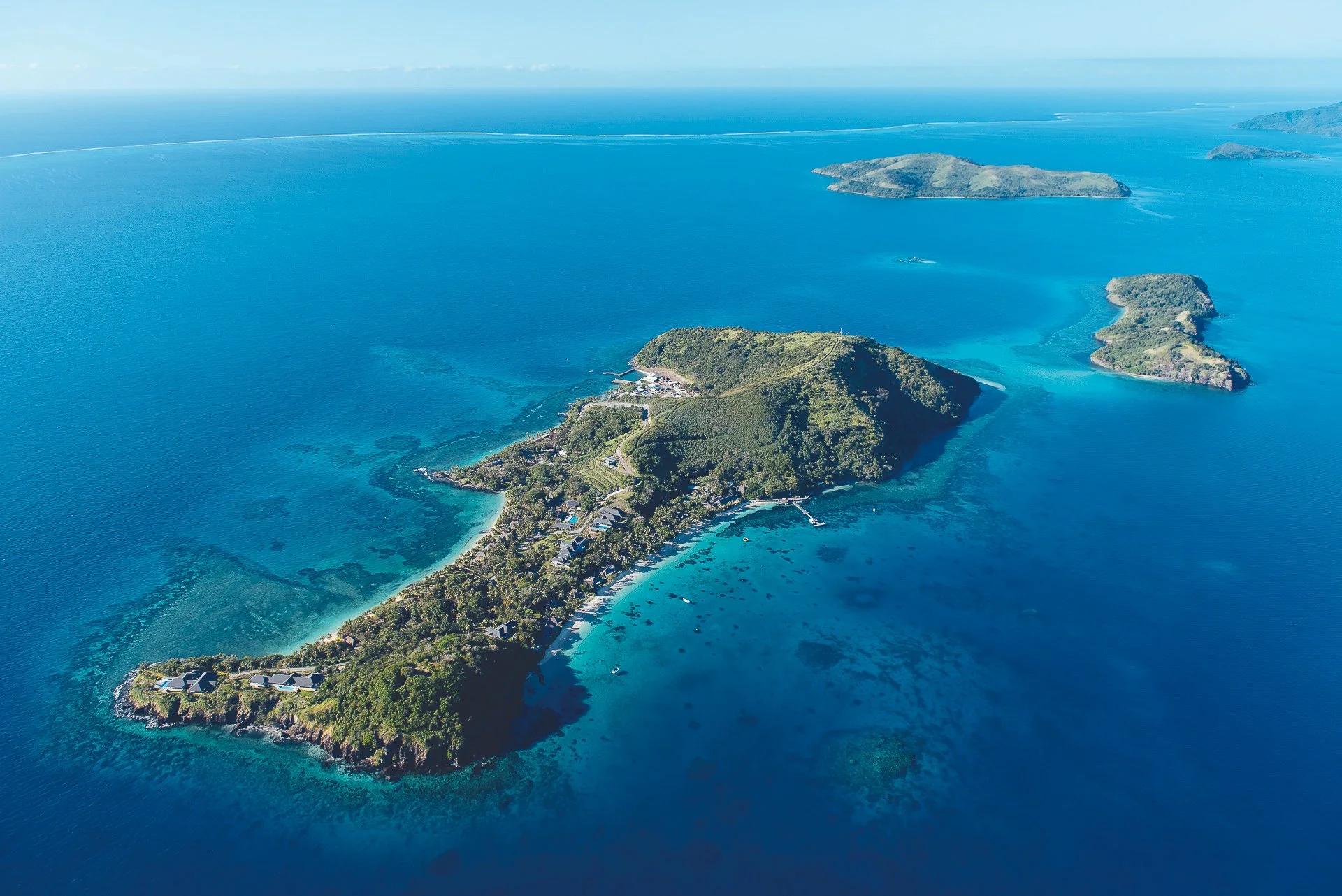 Aerial view of a private island resort in Fiji, with a green ridge, resort villas and turquoise reefs