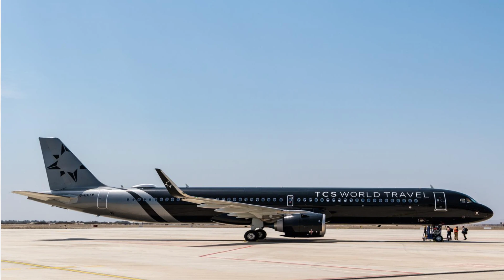 The TCS World Travel private jet, black and silver, parked on the tarmac