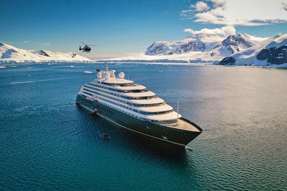 Scenic Eclipse anchored in Antarctica with its helicopter flying above the snowy peaks