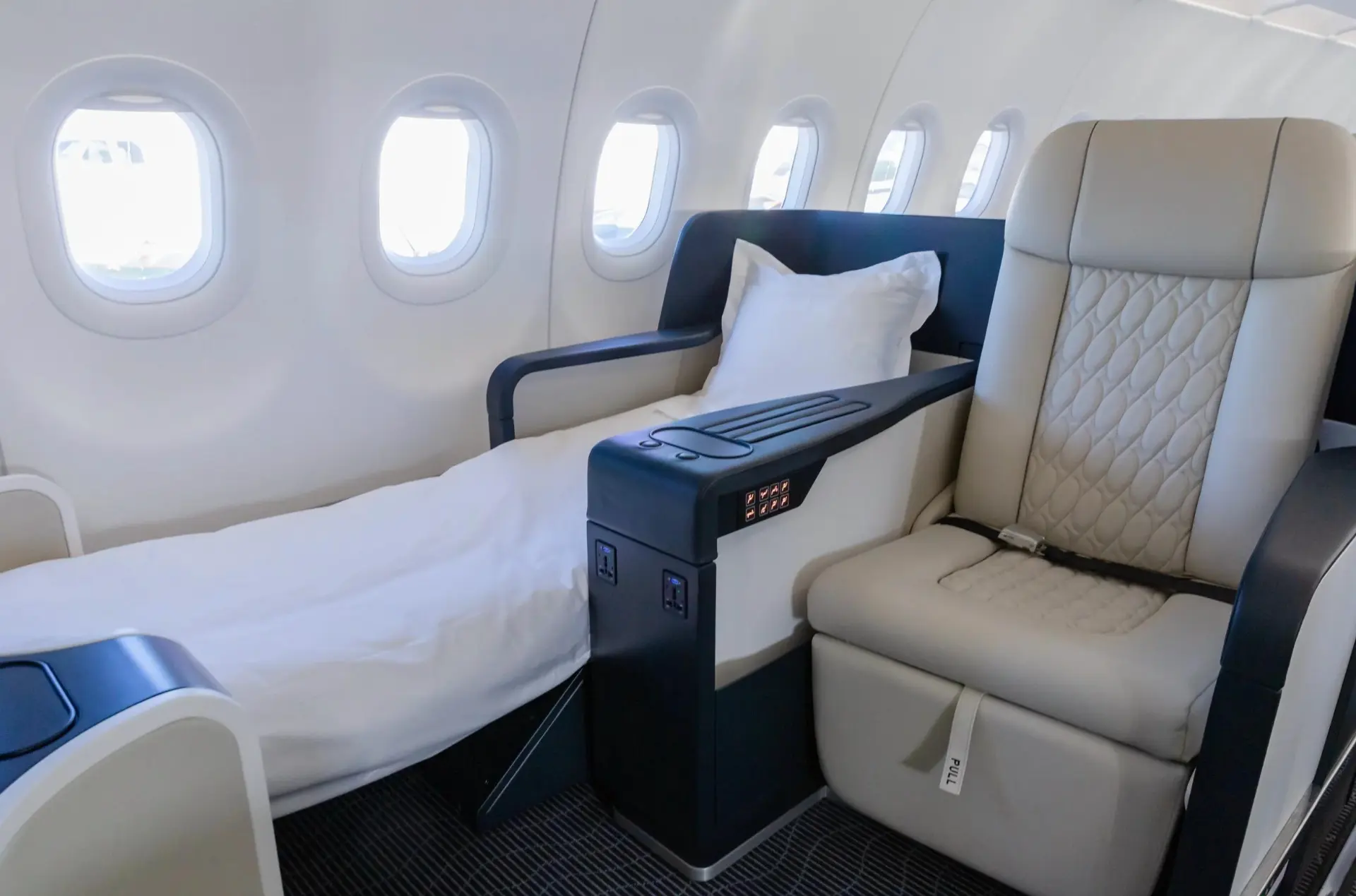 A seat converted to a lie-flat bed with white bedding inside the TCS World Travel jet