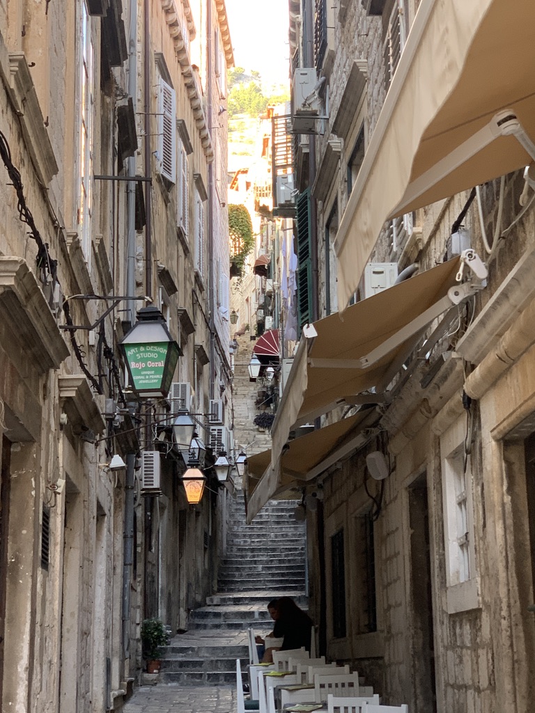 A narrow stone staircase street in the old town of Dubrovnik, Croatia, lined with lanterns and café awnings