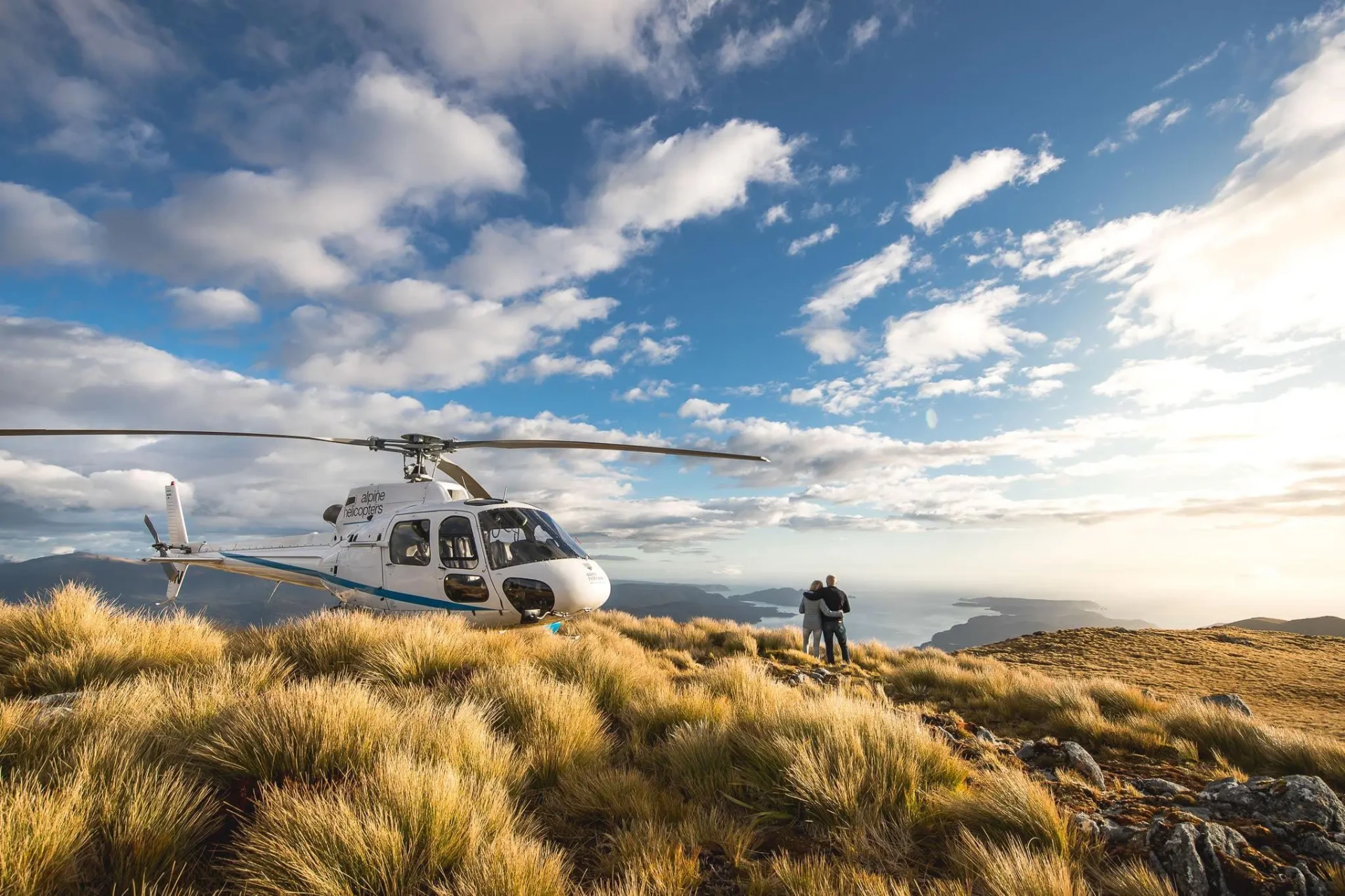 Couple beside a helicopter on a hilltop above the Marlborough Sounds, New Zealand