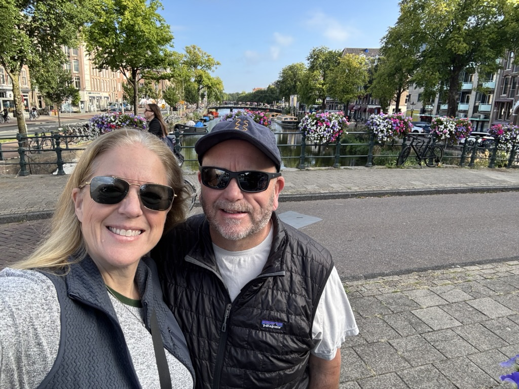 Susan Green and her husband on a canal bridge in Amsterdam, with flower boxes and bicycles along the water