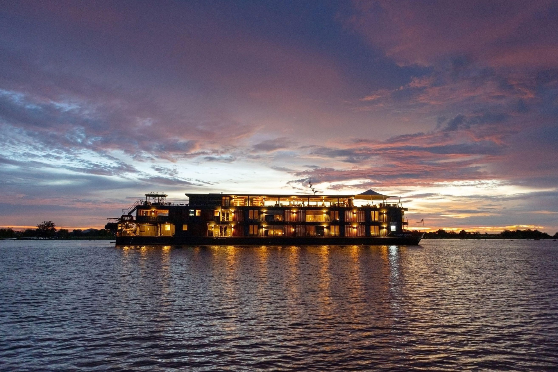 Aqua Expeditions riverboat Aqua Mekong lit up at sunset on the Mekong River